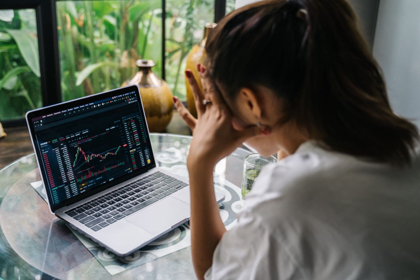 A person holding their head in their hands in front of a laptop showing a financial chart